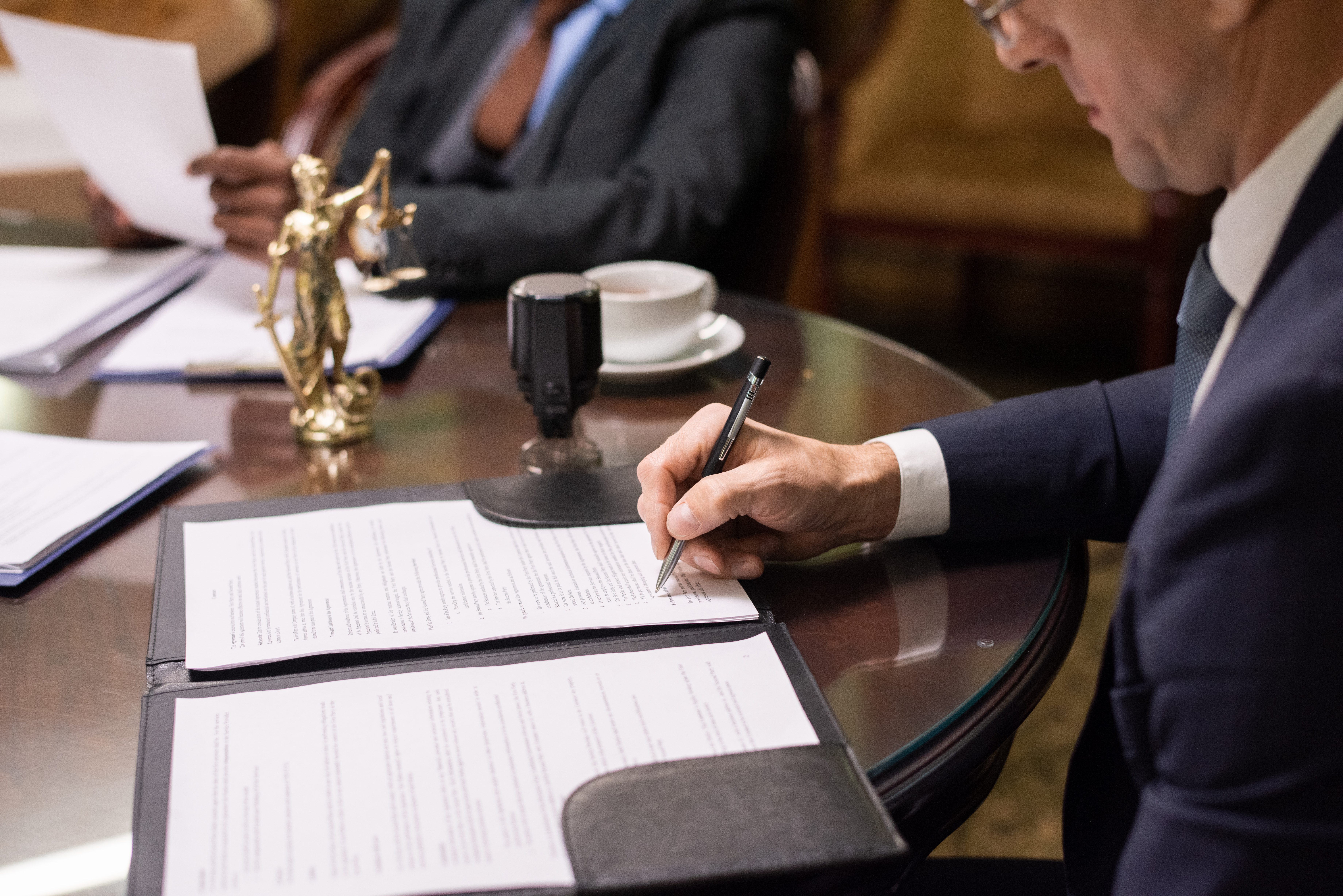 Mature businessman or jurist signing document by workplace